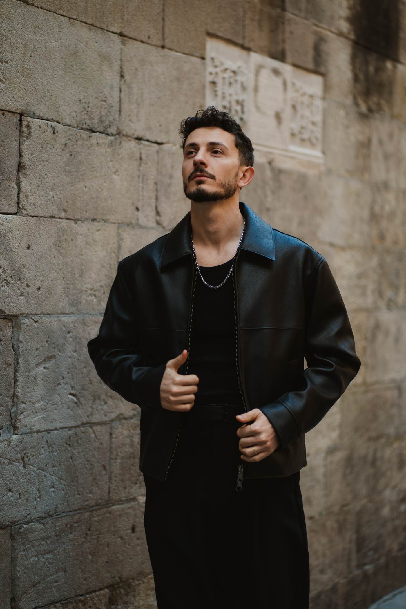 Michael standing against a stone wall in the old town, dressed with intention
