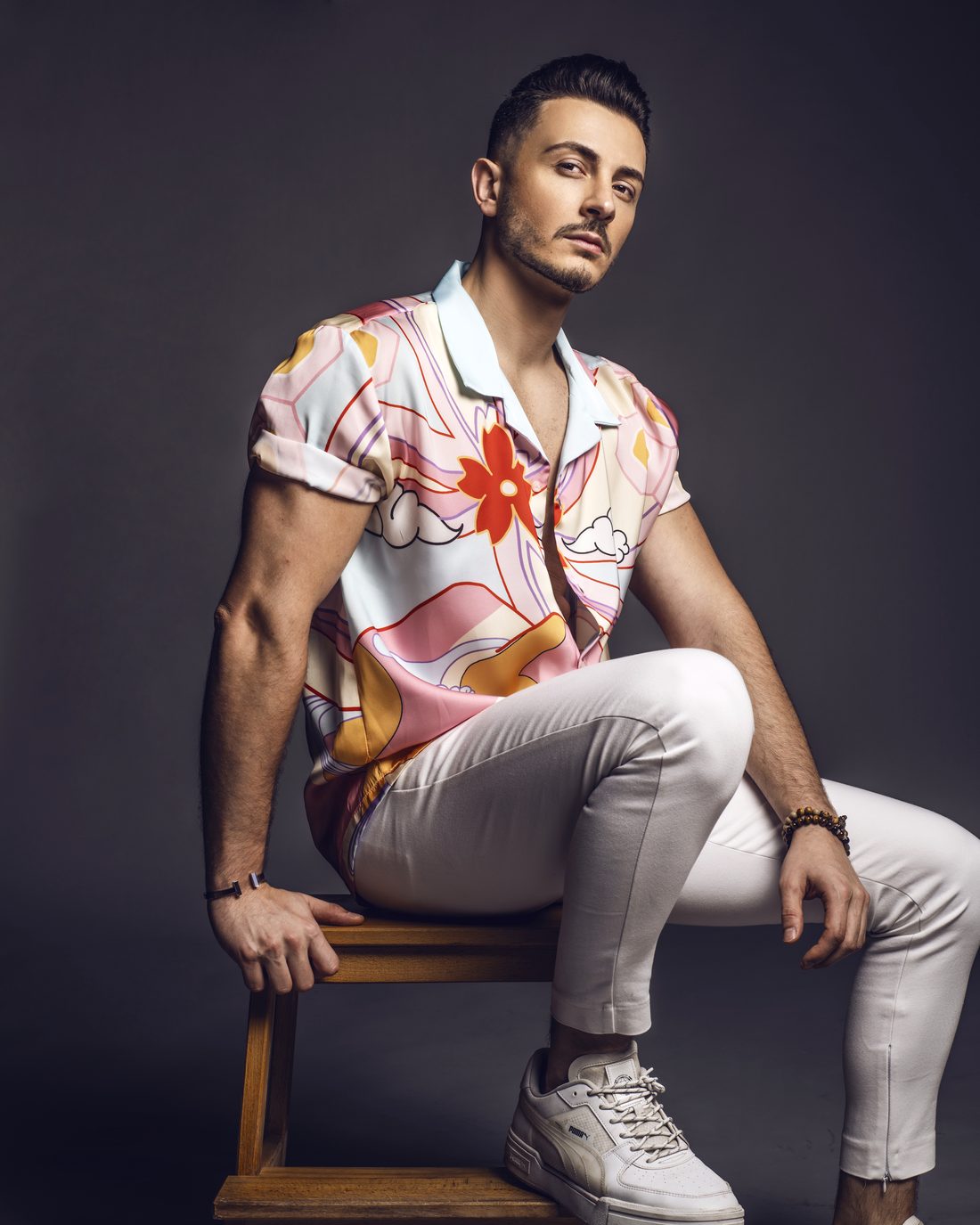 Michael seated on a wooden stool in a floral silk shirt and white trousers